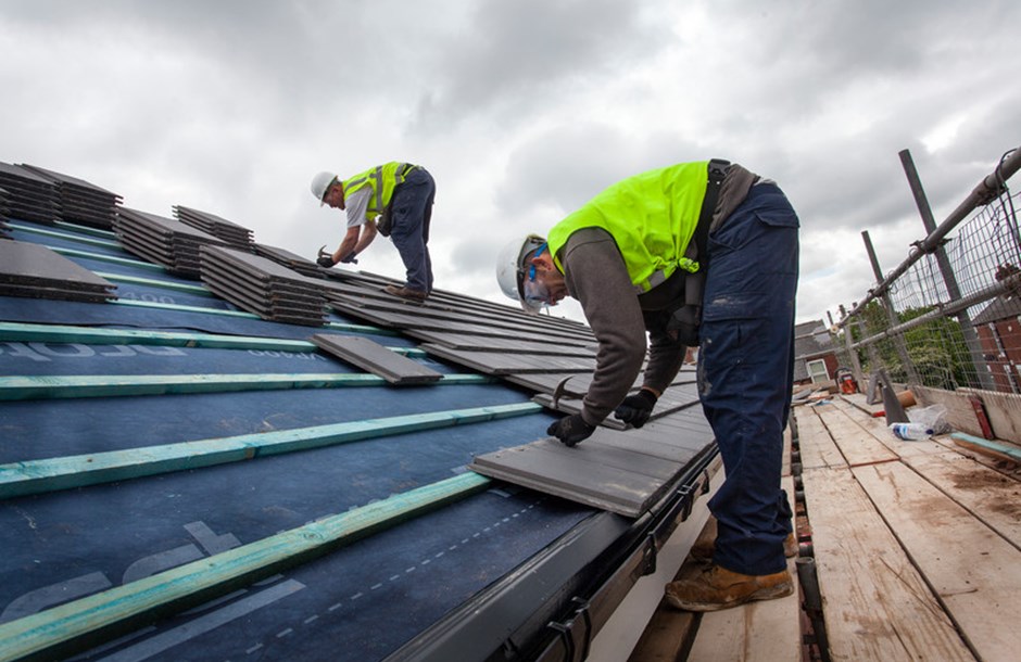 Two construction workers laying tiles on a roof 