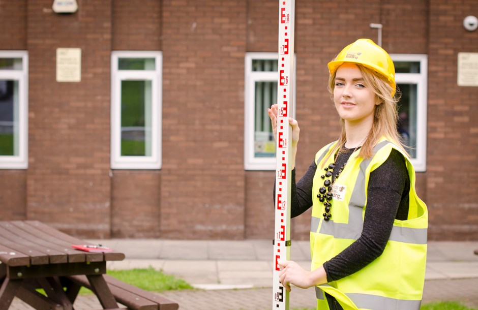 Young woman in hard hat and hi-vis with construction measuring equipment