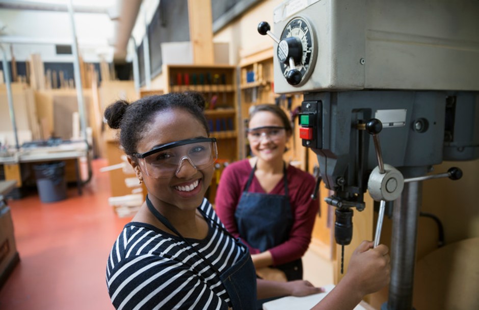 Two apprentices or students with eye protection using equipment in a workshop