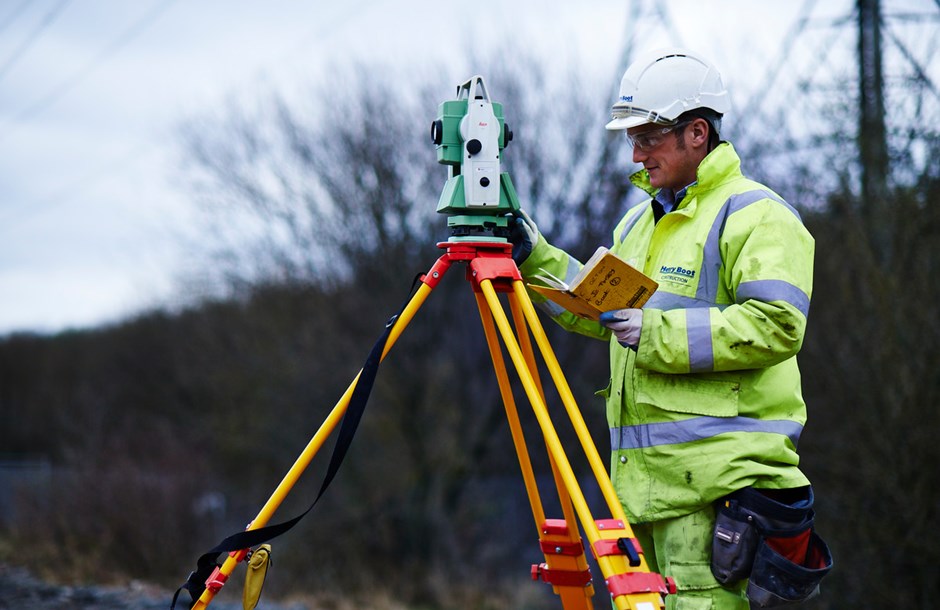 Man in a hi-vis suit and hard hat working with surveying equipment